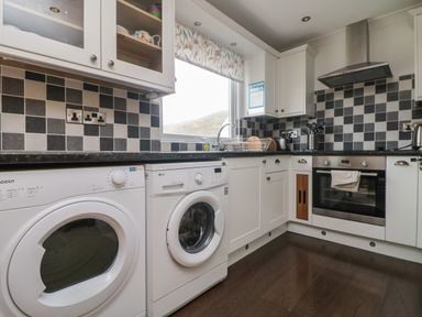 A kitchen with white appliances including a washing machine and oven with black and white tiled backsplash at Ocean Blue in Porthtowan