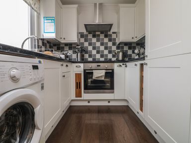 A kitchen with white cabinets black and white checkered backsplash washing machine sink and stainless steel oven at Ocean Blue in Porthtowan