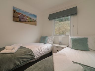 A bedroom with two single beds a window between them and a small bedside table with a lamp at Ocean Blue in Porthtowan