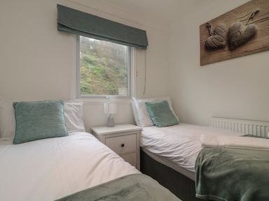 A bedroom with two single beds a nightstand and a window at Ocean Blue in Porthtowan