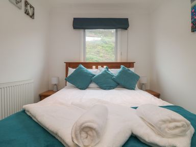 A bedroom with a wooden bed framed with teal pillows and towels at Ocean Blue in Porthtowan