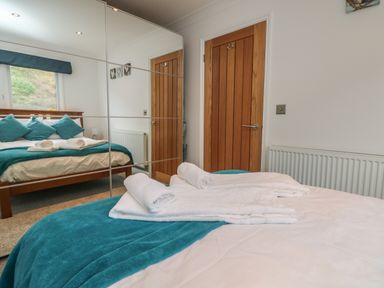 A bedroom with a wooden bed frame dressed with teal and white bedding folded white towels on the bed and mirrored wardrobes at Ocean Blue in Porthtowan