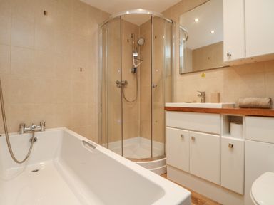A bathroom with a bathtub shower enclosure and a sink with cabinets at Ocean Blue in Porthtowan