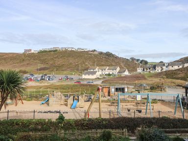 An outdoor playground with slides and swings near a parking lot and houses on a hillside at Ocean Blue in Porthtowan