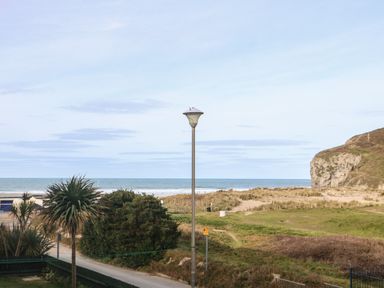 A coastal landscape with a road street lamp bushes and a rocky hill by the sea at Ocean Blue in Porthtowan