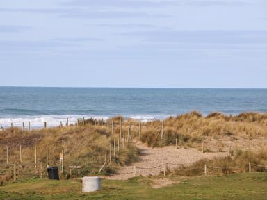 A sandy path through grassy dunes leading to the ocean at Ocean Blue in Porthtowan