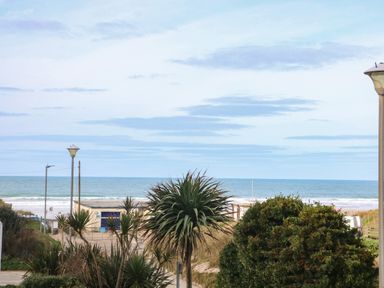 A beach view with palm trees bushes and a building near the ocean at Ocean Blue in Porthtowan