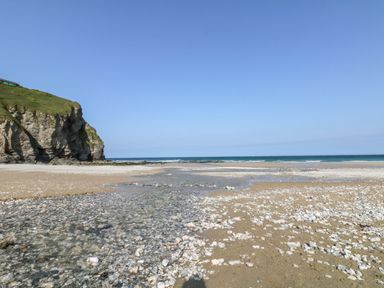 A beach with pebbles and sand with a rocky cliff and ocean in the background at Ocean Blue in Porthtowan