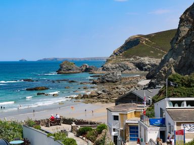 A rocky beach with people on the sand and in the water surrounded by buildings and cliffs at Ocean Blue in Porthtowan