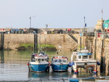 Three boats docked in a harbor with stone walls and fishing equipment on the dock at Bayview in Watergate Bay