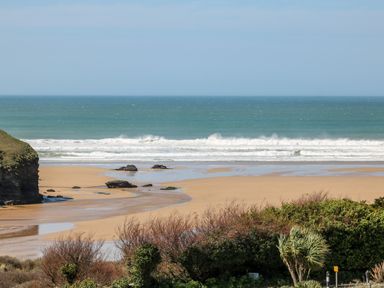 A sandy beach with rocks and waves next to greenery at Bayview in Watergate Bay