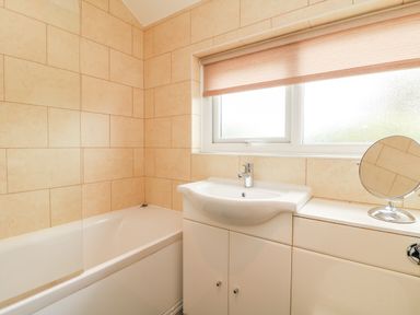 A bathroom with a bathtub sink and a window with a blind at Bayview in Watergate Bay