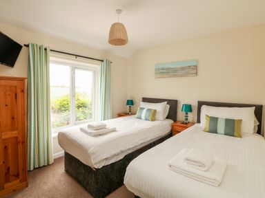 A bedroom with two single beds wooden wardrobe window with curtains and bedside tables with lamps at Bayview Watergate Bay