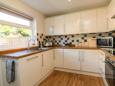 A kitchen with white cabinets wooden countertops a window and colorful tiled backsplash at Bayview in Watergate Bay
