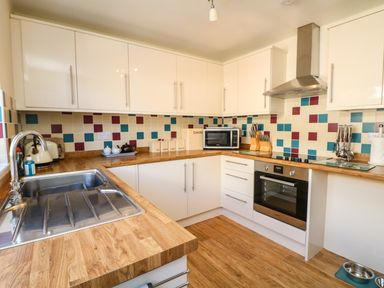 A kitchen with wooden countertops white cabinets a stainless steel sink and oven with colorful tiled backsplash at Bayview in Watergate Bay