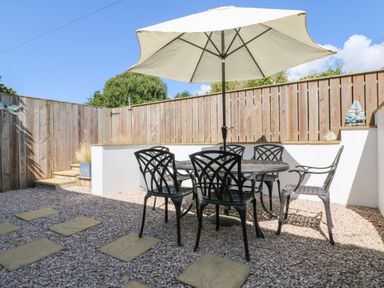 An outdoor patio with a round table and five black chairs under a large umbrella at Bayview in Watergate Bay