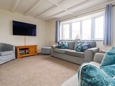 A living room with sofas and cushions a wood TV stand with a TV on the wall and a window with striped curtains at Bayview Watergate Bay