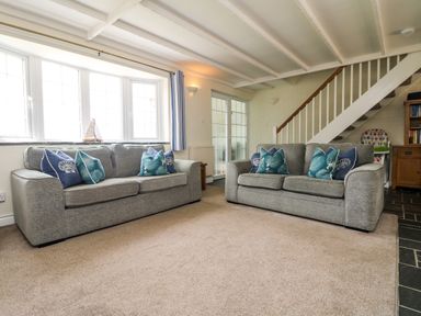 A living room with two grey sofas and blue patterned cushions near a window and stairs at Bayview in Watergate Bay