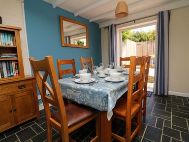 A dining room with a wooden table set for six with white dishes and blue patterned tablecloth at Bayview in Watergate Bay