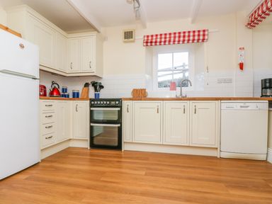 A kitchen with white cabinets stove refrigerator dishwasher and a window with red and white check curtains at Goshen Farm in St Agnes