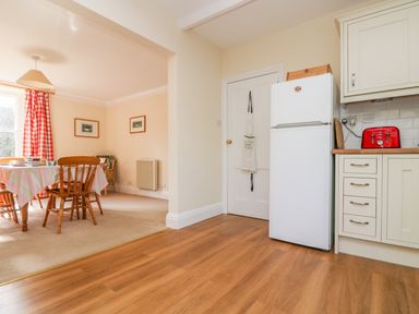 A kitchen with a white fridge red toaster cream cabinets and a dining area with a table chairs and red check curtains at Goshen Farm in St Agnes