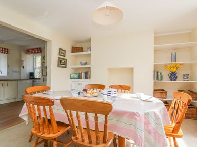 A dining room with a table set for tea and wooden chairs near shelves and a kitchen at Goshen Farm in St Agnes