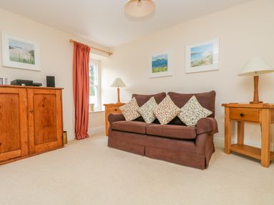 A living room with a brown sofa with patterned cushions wooden side tables with lamps wooden cabinet and framed pictures on the wall at Goshen Farm in St Agnes