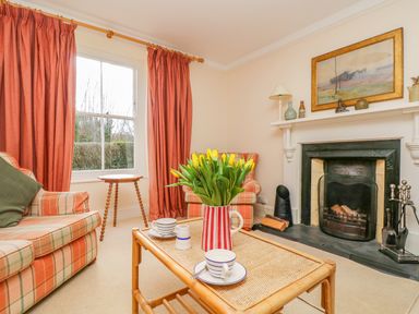 A living room with a fireplace a coffee table with flowers and cups and plaid sofas with curtains at Goshen Farm in St Agnes