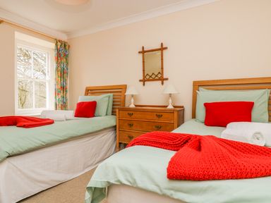 A bedroom with two single beds with red pillows and blankets a wooden dresser with two lamps and a mirror at Goshen Farm in St Agnes