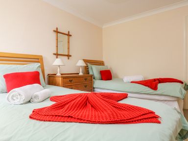 A bedroom with two single beds with red pillows and blankets a wooden dresser with two lamps and a mirror on the wall at Goshen Farm in St Agnes