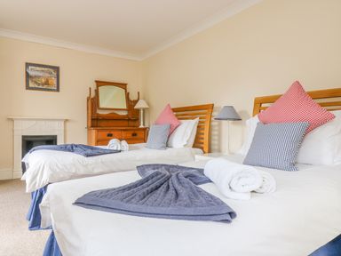 A bedroom with two single beds with cushions a wooden dresser with a mirror and a small fireplace at Goshen Farm in St Agnes