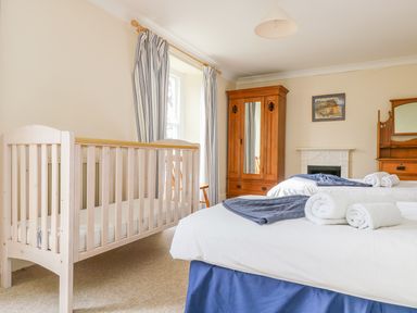 A bedroom with a wooden crib twin beds with towels and blankets a wooden wardrobe and dresser at Goshen Farm in St Agnes