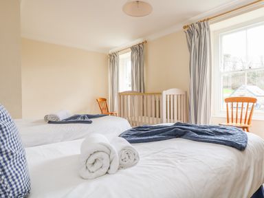 A bedroom with two single beds a wooden crib two wooden chairs and curtained windows at Goshen Farm in St Agnes