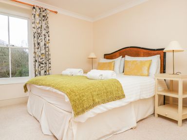 A bedroom with a bed with yellow pillows and a green throw with a bedside table and lamp at Goshen Farm in St Agnes
