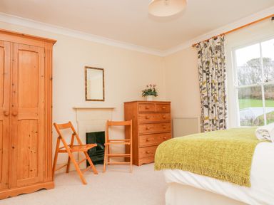 A bedroom with wooden wardrobe, two wooden chairs, chest of drawers, and a bed with green blanket at Goshen Farm in St Agnes