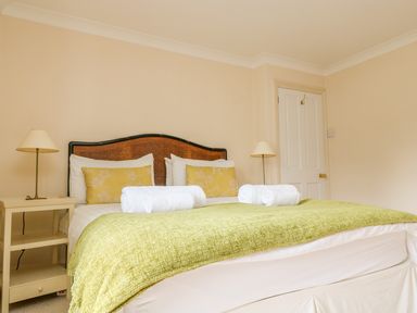A bedroom with a bed with green cover and yellow pillows with two lamps on bedside tables at Goshen Farm in St Agnes