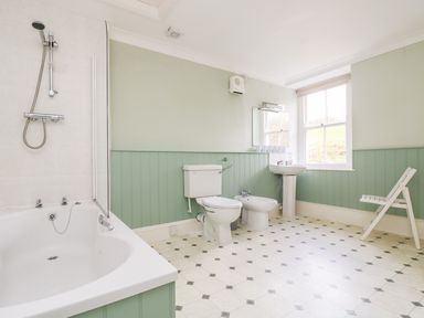 A bathroom with a bathtub shower toilet bidet sink mirror white chair and window at Goshen Farm in St Agnes
