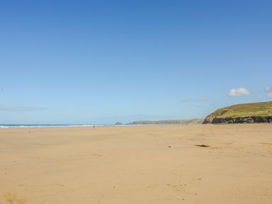 A wide sandy beach with the ocean on the left and grassy cliffs on the right at Goshen Farm in St Agnes
