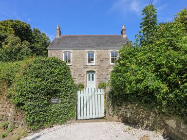 A stone house behind a white wooden gate with green ivy on the walls at Goshen Farm in St Agnes