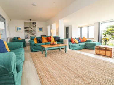 A living room with green sofas colorful cushions a wooden coffee table and large windows at Trelawns in Mawgan Porth