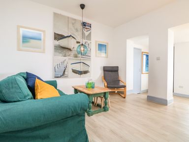 A living room with a green sofa yellow and blue cushions a wooden coffee table and a gray armchair at Trelawns in Mawgan Porth