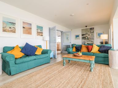 A living room with green sofas and colorful cushions a wooden coffee table and framed pictures on the walls at Trelawns in Mawgan Porth