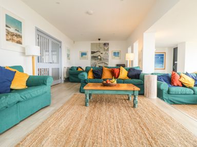 A living room with teal sofas and colorful cushions with a wooden coffee table on a woven rug at Trelawns in Mawgan Porth