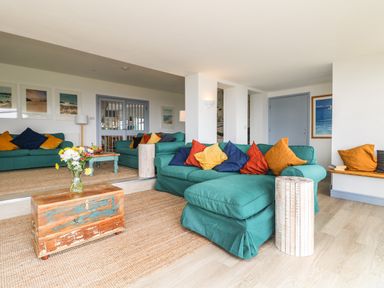 A living room with teal sofas and multicolored cushions a wooden chest with flowers on it and a bench with cushions at Trelawns in Mawgan Porth