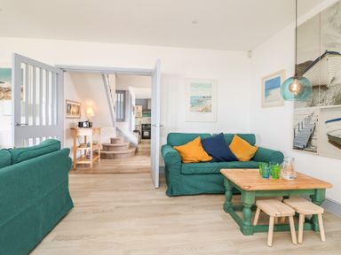 A living room with green sofas a wooden coffee table and stools a small table with a lamp and stairs in the background at Trelawns in Mawgan Porth