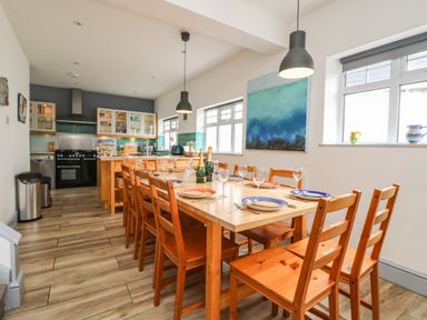 A kitchen with a wooden dining table set for eight people and pendant lights at Trelawns in Mawgan Porth