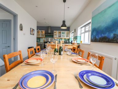 A dining table set with colorful plates and glasses in a kitchen at Trelawns in Mawgan Porth
