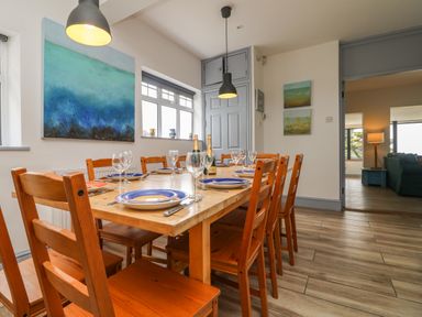 A dining room with a wooden table set with plates and glasses and wooden chairs at Trelawns in Mawgan Porth
