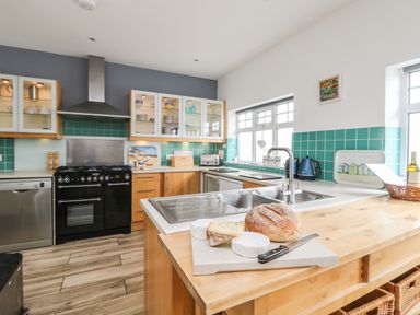 A kitchen with wooden cabinets a black oven and range a stainless steel dishwasher and a counter with cheese and bread at Trelawns in Mawgan Porth