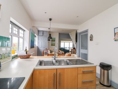 A kitchen with wooden cabinets a double sink and a dining table with chairs at Trelawns in Mawgan Porth